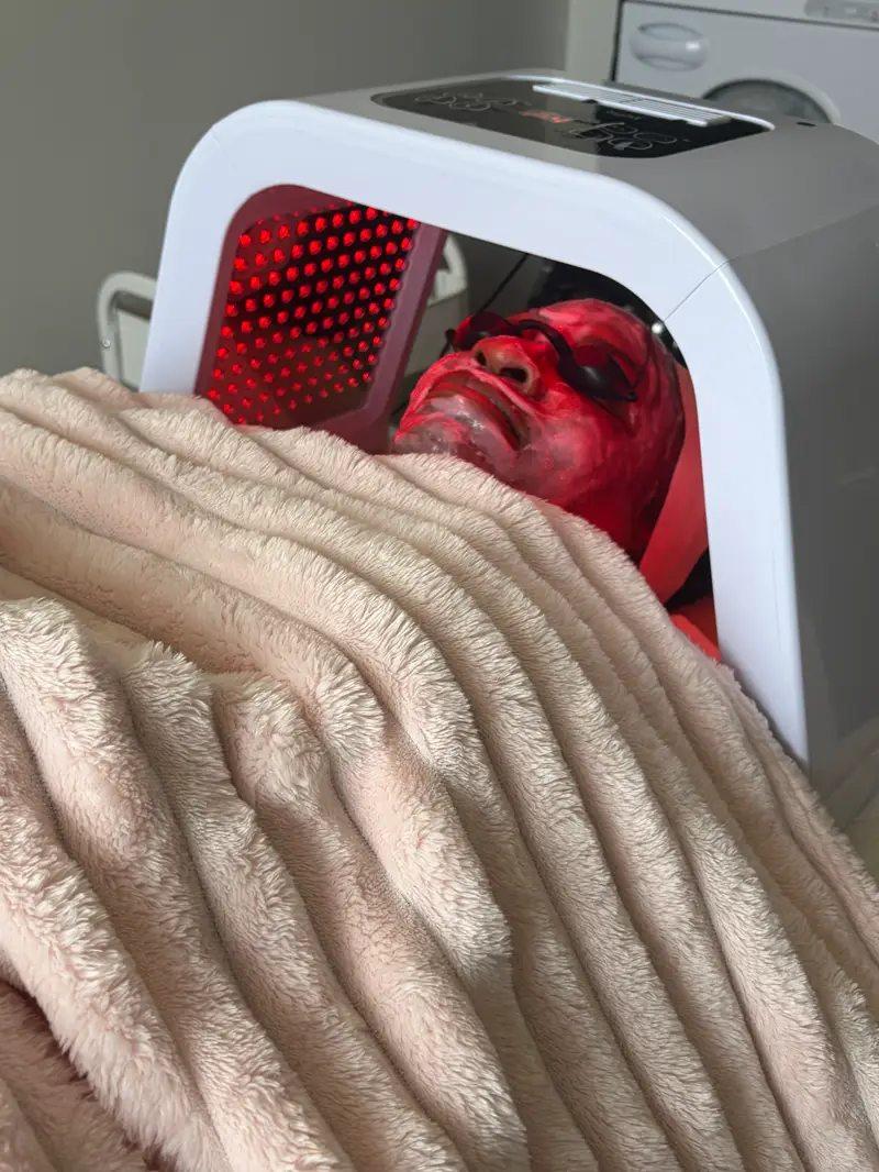 Client under red LED light therapy, wrapped in a soft blush blanket